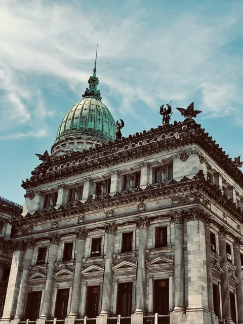 An ornate Buenos Aires building with a green dome beneath a cloudy sky.