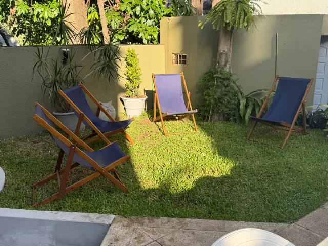 Three deckchairs on a sunny patch of grass surrounded by garden plants.